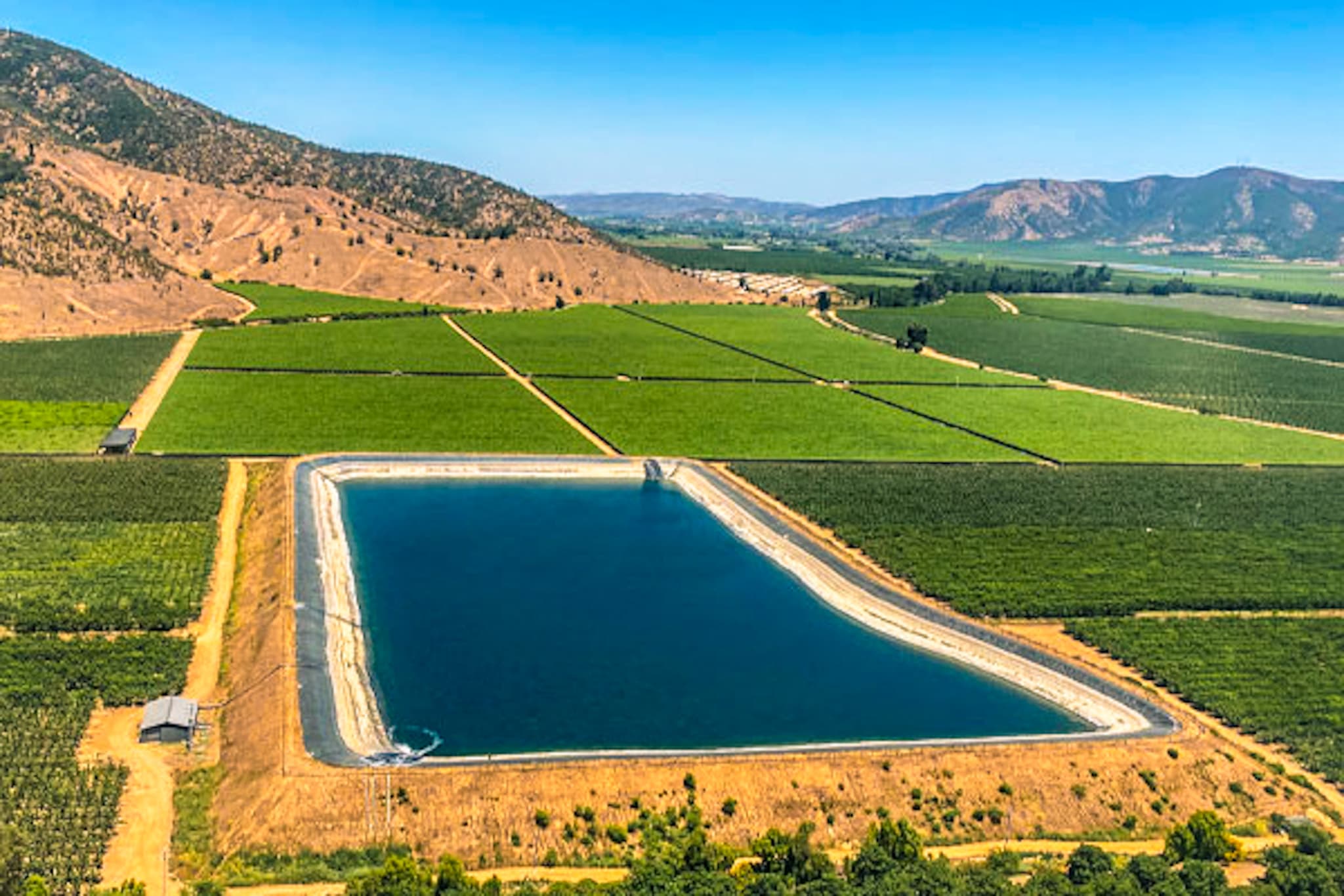 Vista aérea de campos agrícolas con reservorio de agua en valle central